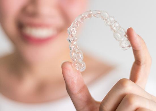 Woman blurry in background holding clear aligner to foreground