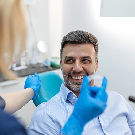 Man in dental chair smiling at dentist holding clear aligner
