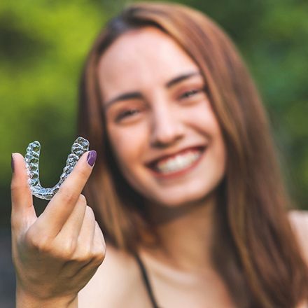 Woman outside smiling holding clear aligner
