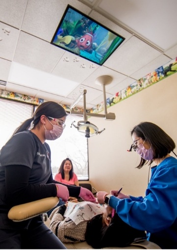 Dental team member and dentist treating dental patient observed by parent