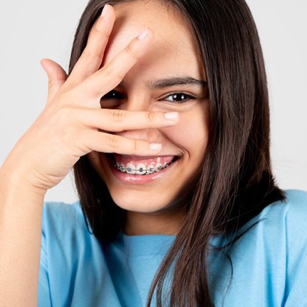 Child holding her hand over her face and smiling with braces