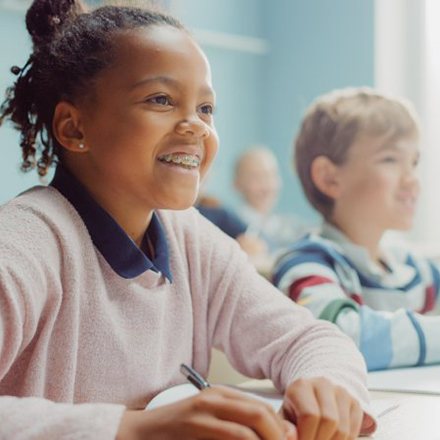 Child with braces at her school desk listens attentively 