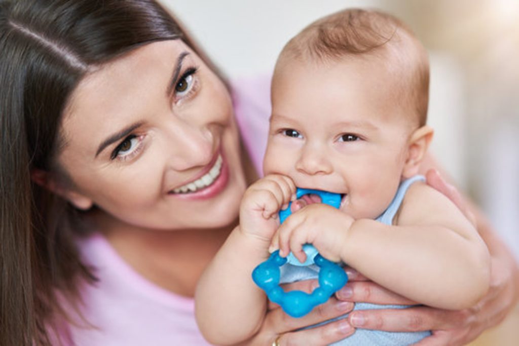 parent smiling and holding baby using a teething ring 